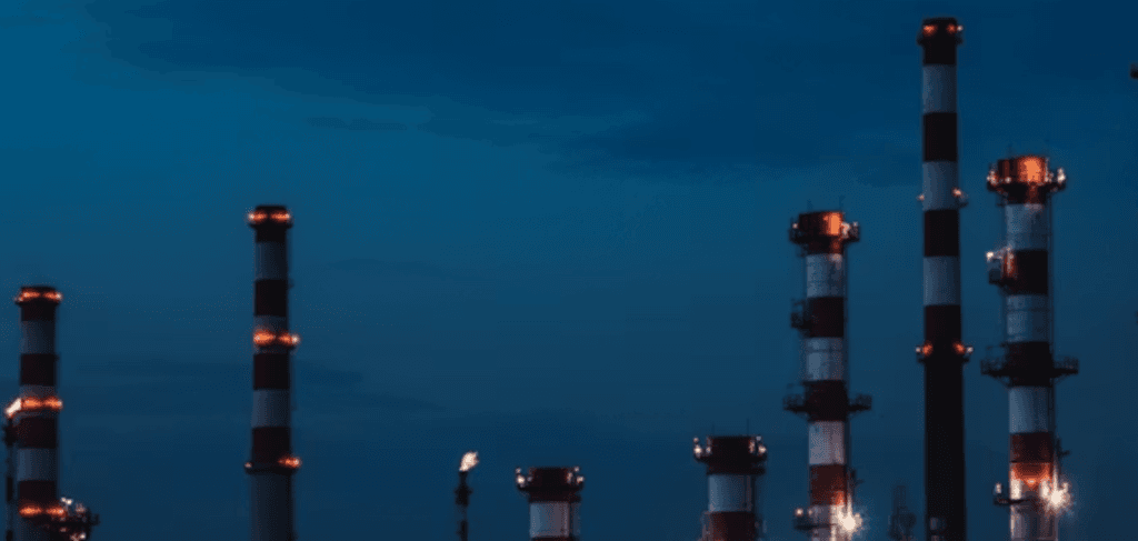 Industrial facility towers and smokestacks under a deep blue twilight sky